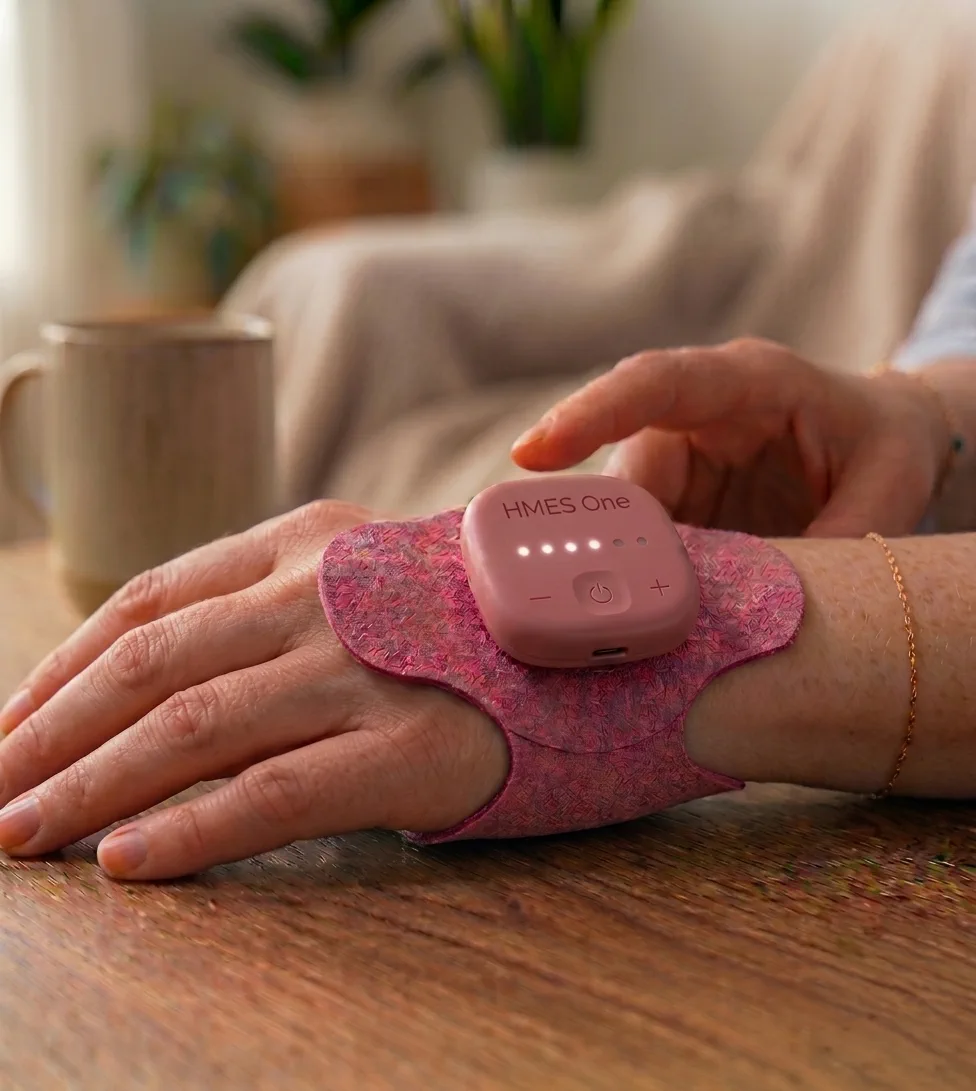 The Myogen HMES One device worn on the back of a woman's hand, resting on a wooden table at home.
